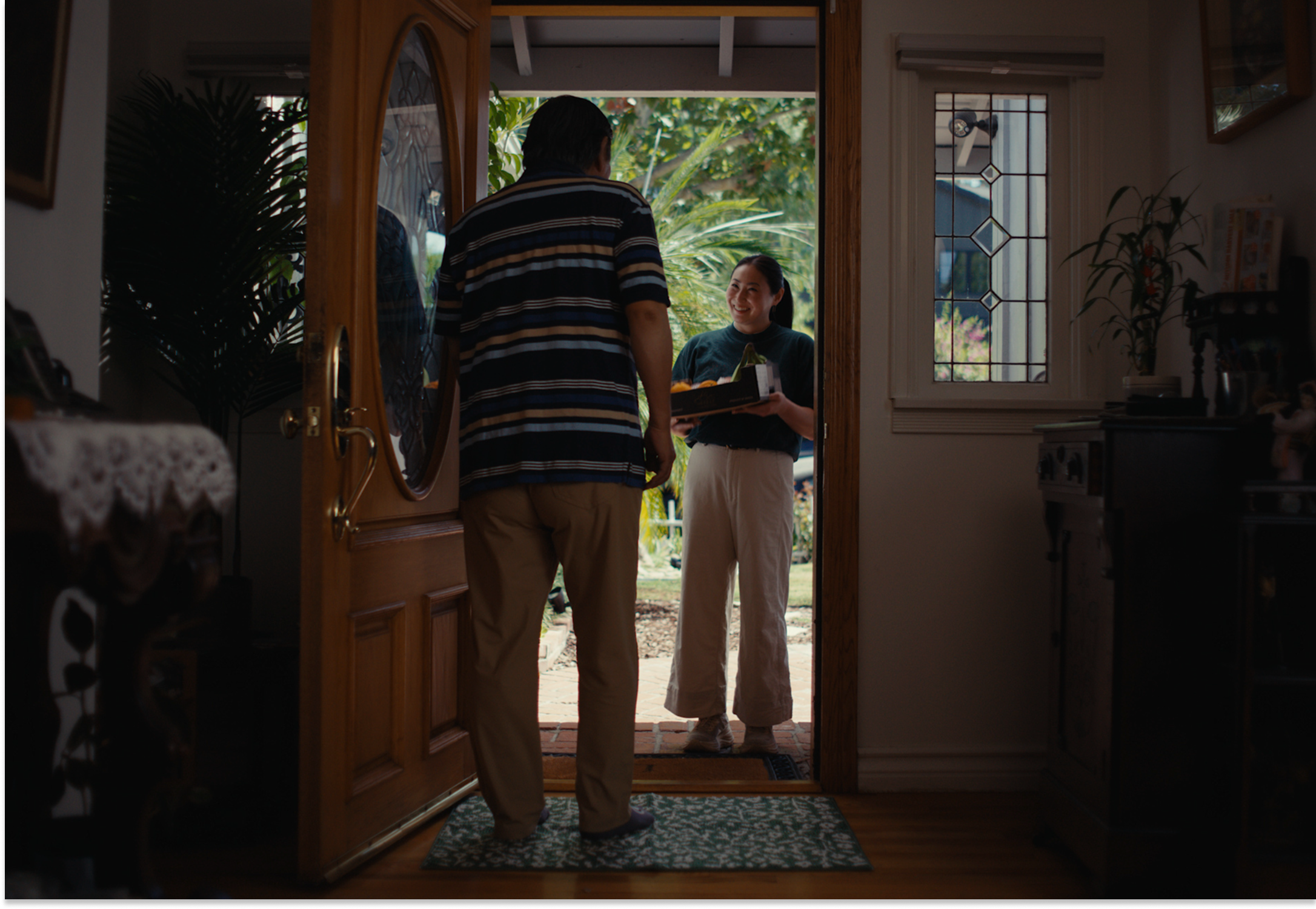 A visitor at the door holding a gift of green bananas